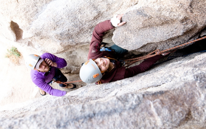 two students in rock climbing gear smile at the camera while navigating a crag 